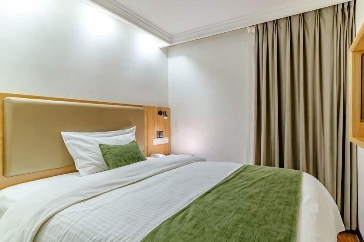 A hotel room with a bed, a headboard, a nightstand, a lamp, and a window with curtains.
