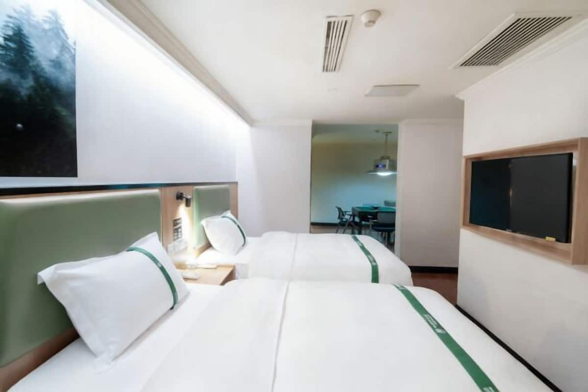 A hotel room with two beds, a desk, a chair, and a large window.