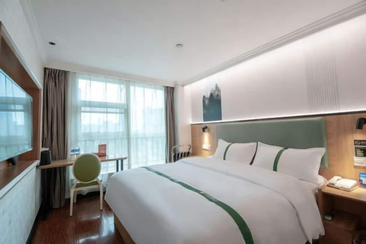 A hotel room with a large bed, a desk, a chair, a TV, and a window with curtains.