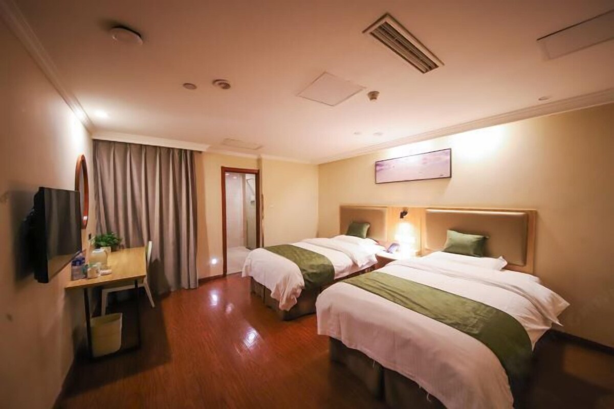 Een hotelkamer met twee bedden, een bureau, een stoel, een televisie en een deur naar een andere kamer.