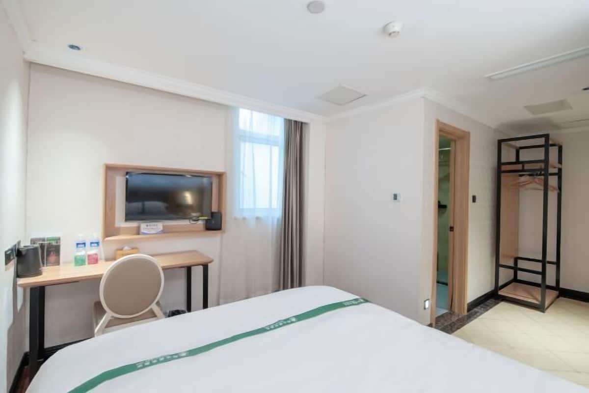 A hotel room with a bed, a desk with a chair, a television, and a wardrobe.