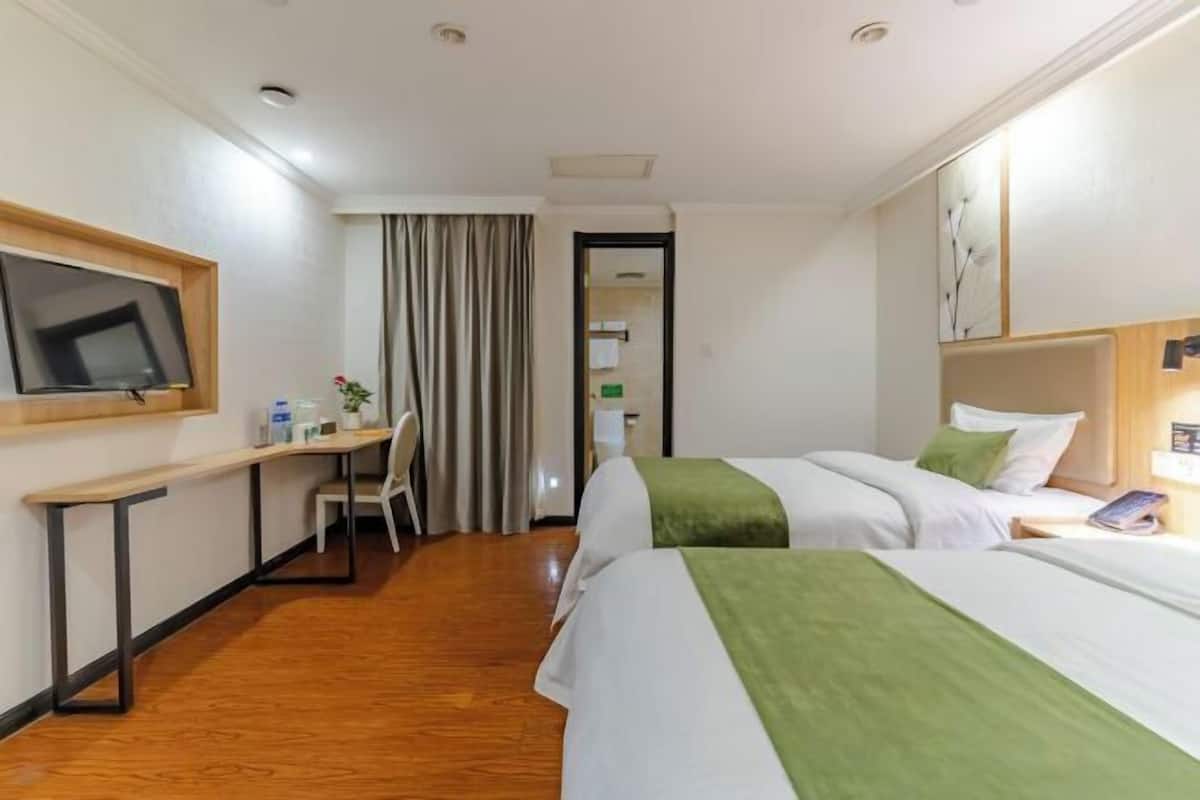A hotel room with two beds, a desk, a chair, a television, and a door leading to a bathroom.