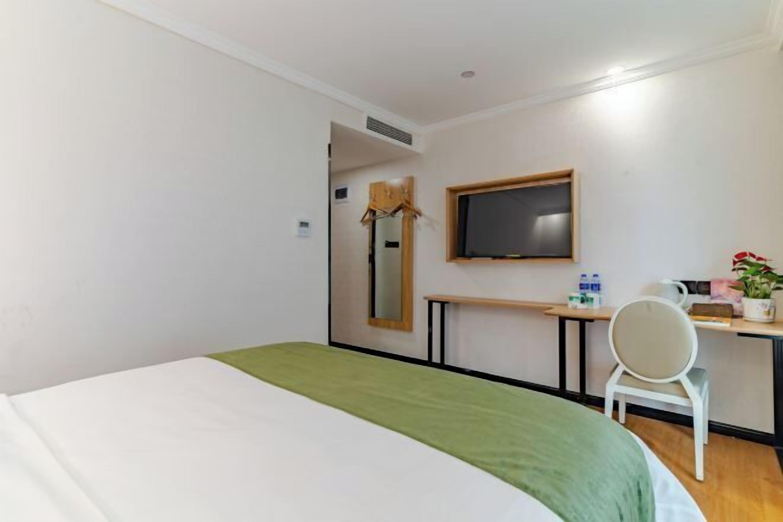 A hotel room with a bed, a desk with a chair, a television, and a small table with a plant.