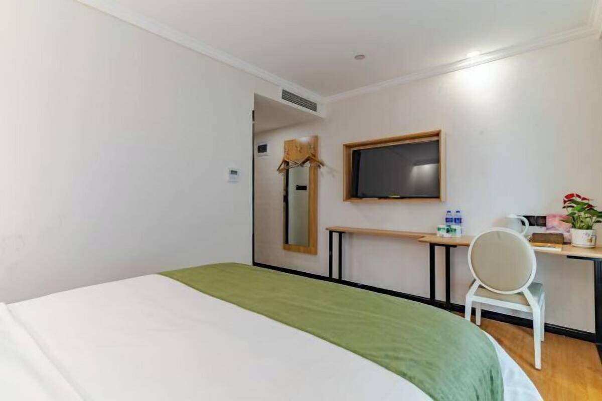 A hotel room with a bed, a desk with a chair, a television, and a small table with a plant.