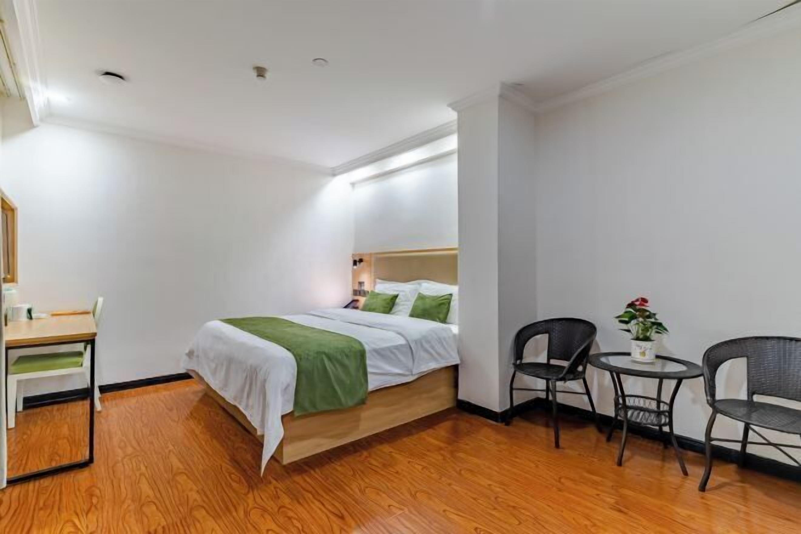 Habitación de hotel con cama, escritorio, dos sillas, una mesita y una planta en maceta.