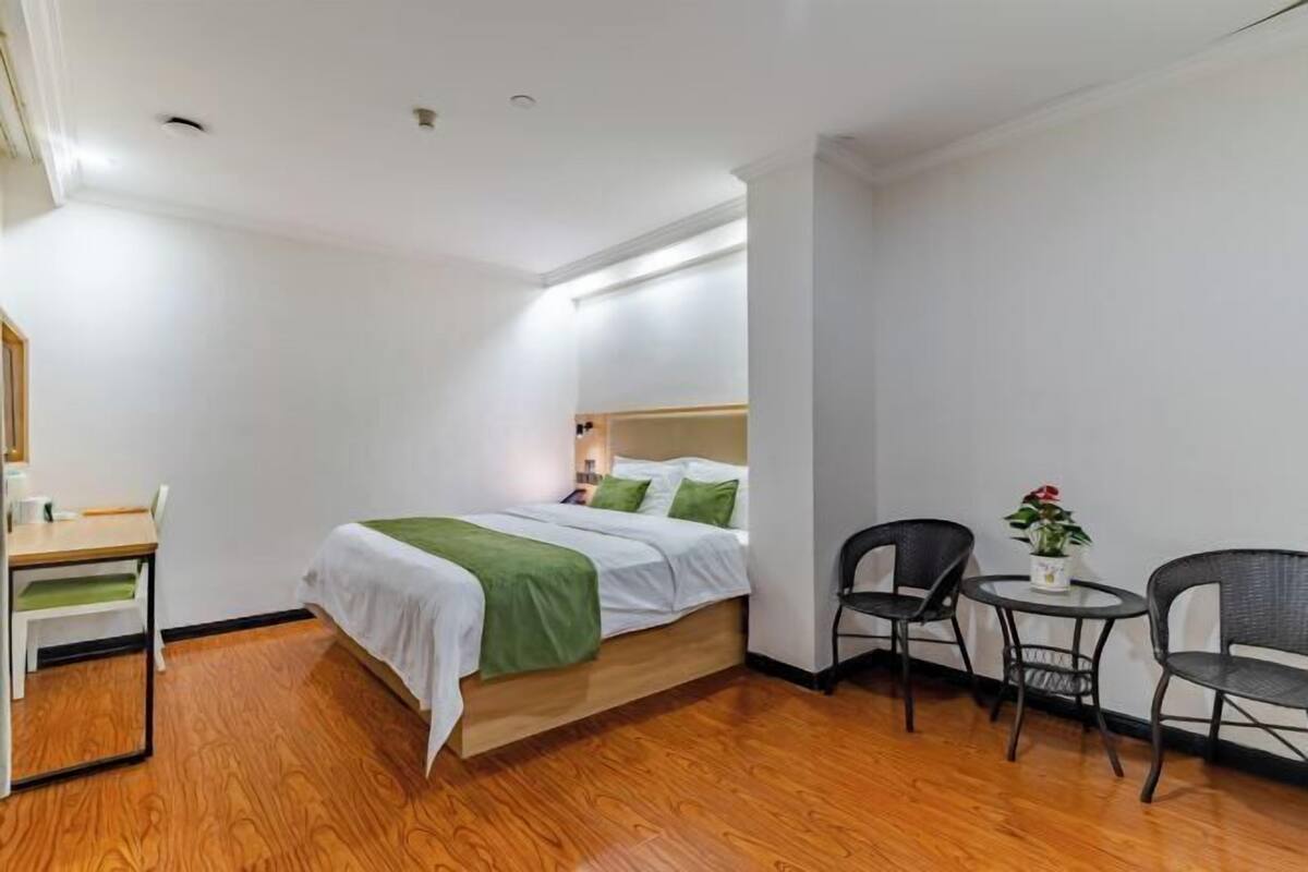A hotel room with a bed, a desk, two chairs, a small table, and a potted plant.