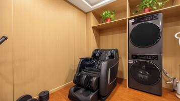 A room with a massage chair, a washing machine, and a shelf with plants.