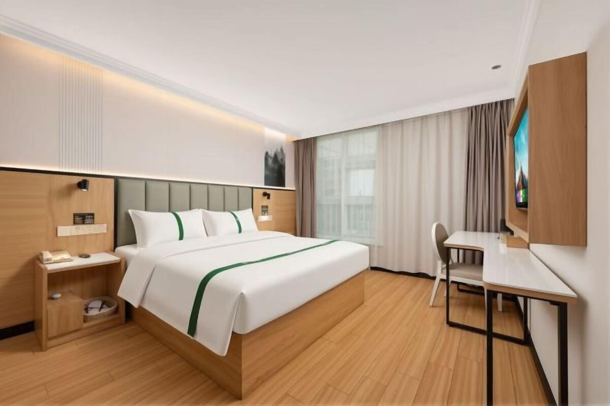 Una camera d'albergo con un letto, comodino, sedia, scrivania e un'ampia finestra con tende.