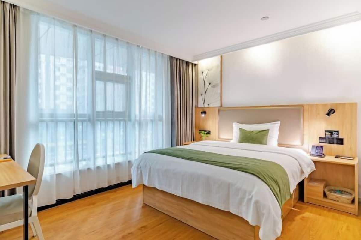 A hotel room with a large bed, a desk, and a window with sheer curtains.