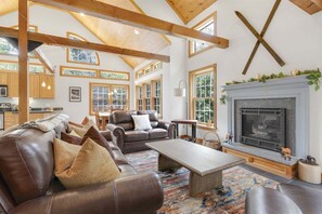 A spacious living room with a fireplace, leather sofas, and a large window overlooking the outdoors.