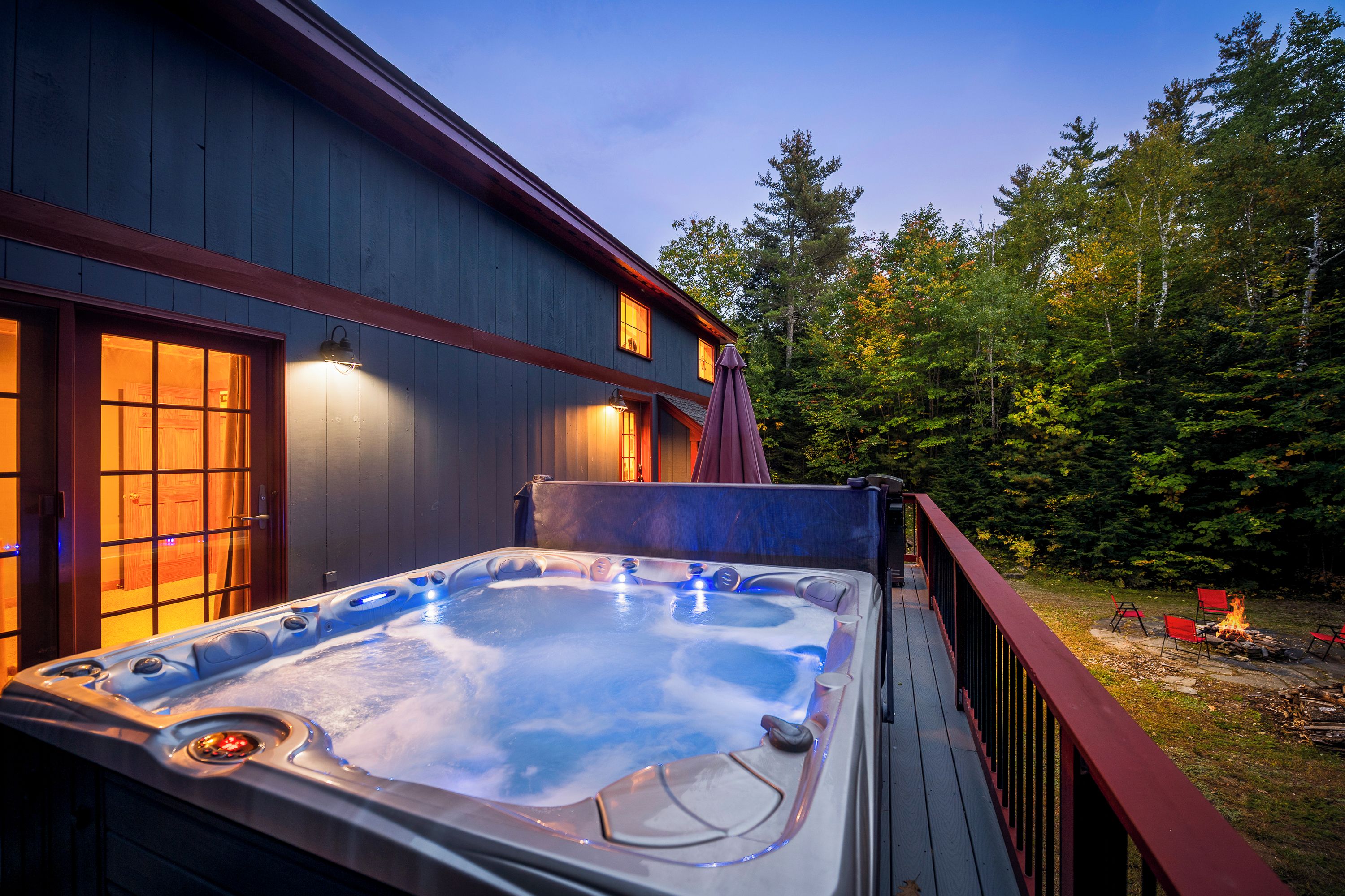 Un bain à remous sur une terrasse en bois, avec vue sur une forêt et un bâtiment doté de fenêtres.