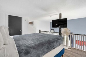 Un dormitorio con cama, televisor en la pared, ventilador y una puerta.