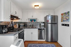 Una cocina moderna con gabinetes blancos, electrodomésticos de acero inoxidable, microondas, tostadora y refrigerador.