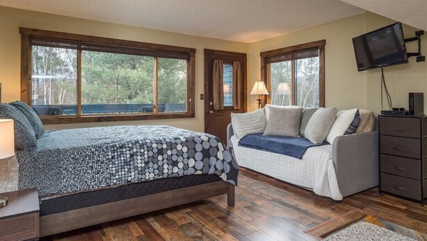 A bedroom with a bed, a sofa, a TV, and large windows.