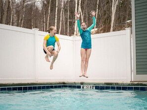 Two people jumping into a swimming pool with a white fence and trees in the background. - Brookside II A-215 - Sunday River Condo (Newry)