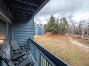A balcony with outdoor furniture, a view of a building, and a wooded area. - Brookside II A-215 - Sunday River Condo (Newry)
