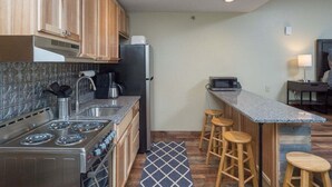 A compact kitchen with a stove, sink, and bar stools.