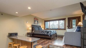 A compact room with a bed, a small kitchenette, a bar area with stools, and a sofa.
