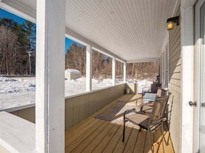 A covered porch with a view of a snowy landscape, wooden flooring, and a door to the right. - Sunday River Getaway (Newry)