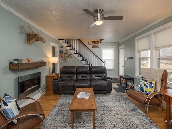 A living room with a fireplace, a black leather sofa, a wooden coffee table, and a brown leather armchair. - Sunday River Getaway (Newry)