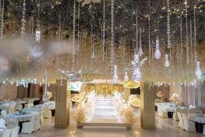 An indoor venue with tables arranged in rows, a central aisle leading to a stage, and hanging crystal-like decorations. - Xingpeng International Hotel (Huayuan)