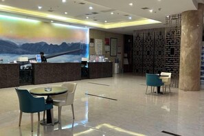 Zona de recepción de un hotel con mostrador, sillas y un gran mural en la pared.