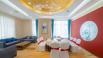 A hotel room with a round dining table, white chairs, a sofa, and a red accent wall.