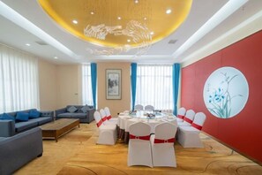 A hotel room with a round dining table, white chairs, a sofa, and a red accent wall. - Xingpeng International Hotel (Huayuan)