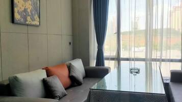 A room with a glass-top table, a sofa with cushions, and a view through large windows.