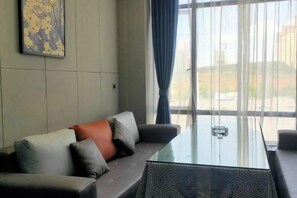 A room with a glass-top table, a sofa with cushions, and a view through large windows. - Xingpeng International Hotel (Huayuan)