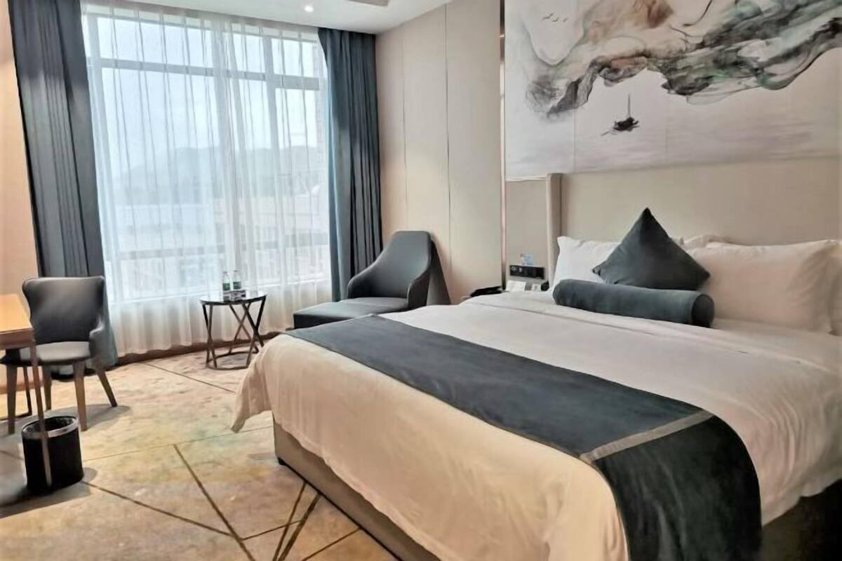 A hotel room with a large bed, two chairs, a small table, and a painting on the wall.