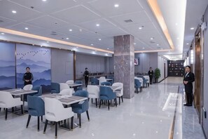 A modern restaurant with tables and chairs, a marble pillar, and a mural on the wall. - Xingpeng International Hotel (Huayuan)