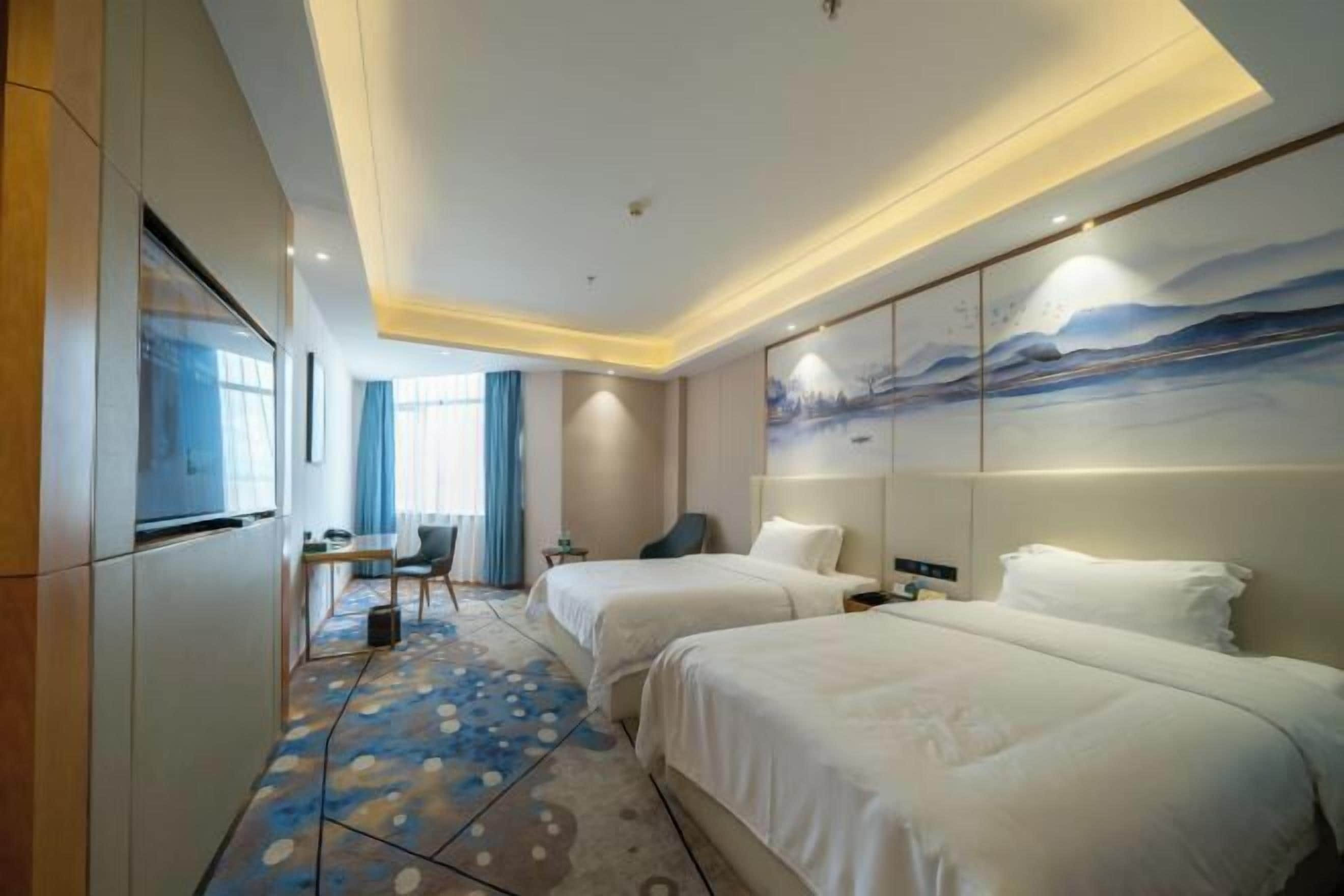 A hotel room with two beds, a desk, a chair, and a painting on the wall.