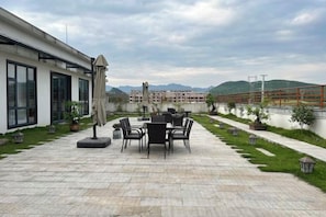 An outdoor patio with a table and chairs, a covered area, and a view of mountains in the distance. - Xingpeng International Hotel (Huayuan)