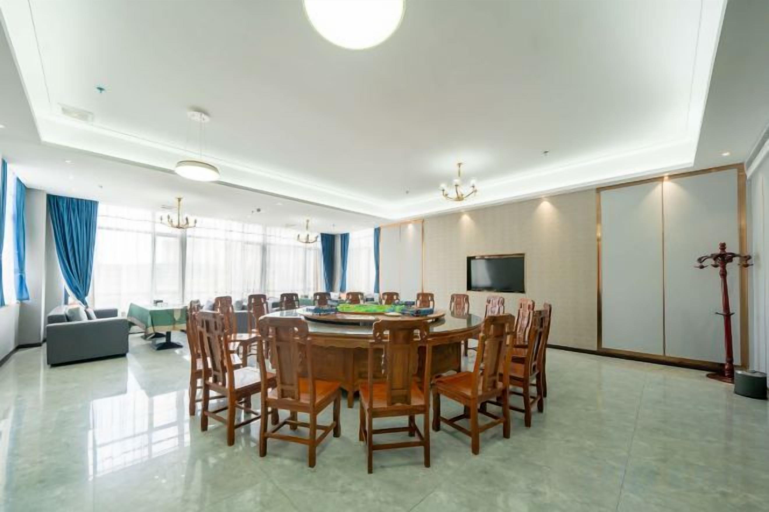 A spacious dining area with a round table and chairs, a sofa, and a television on the wall.