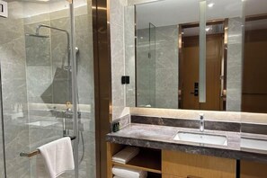 A modern bathroom with a glass-enclosed shower, a large mirror, and a marble countertop. - Xingpeng International Hotel (Huayuan)