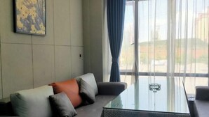A modern living room with a sofa, a glass coffee table, and a large window with curtains. - Xingpeng International Hotel (Huayuan)