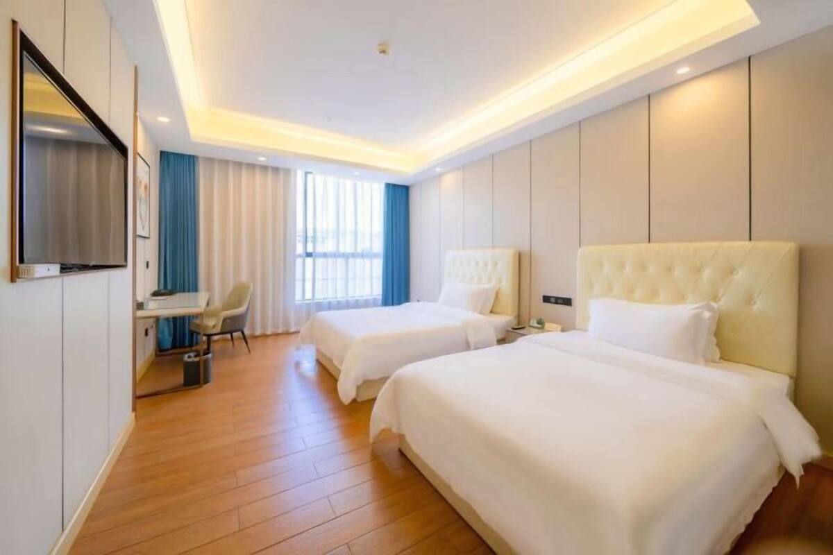 A hotel room with two beds, a desk, and a TV.