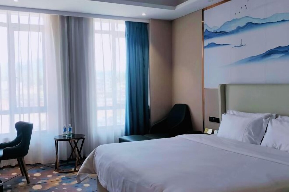 Habitación de hotel con cama, una silla, una mesita y un cuadro en la pared.