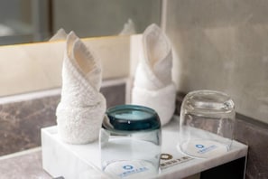 Un baño con encimera de mármol, un tarro de vidrio y un tozalenguas con toallas dobladas.
