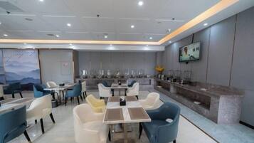 A modern dining area with tables and chairs, a counter with a display, and a wall-mounted television.
