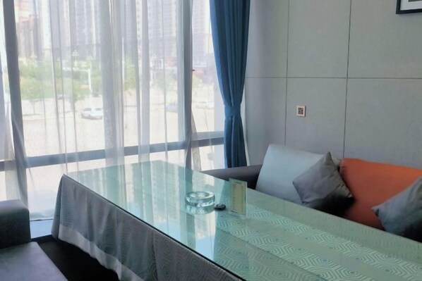 Una habitación moderna con una mesa de vidrio, un sofá con cojines y vistas a la calle a través de amplias ventanas.