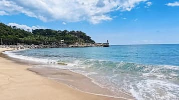 A beach with a clear sky, calm sea, and a lighthouse in the distance.