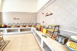 Disposição de buffet com várias estações de comida, um dispensador de bebidas de serviço livre e uma torradeira.