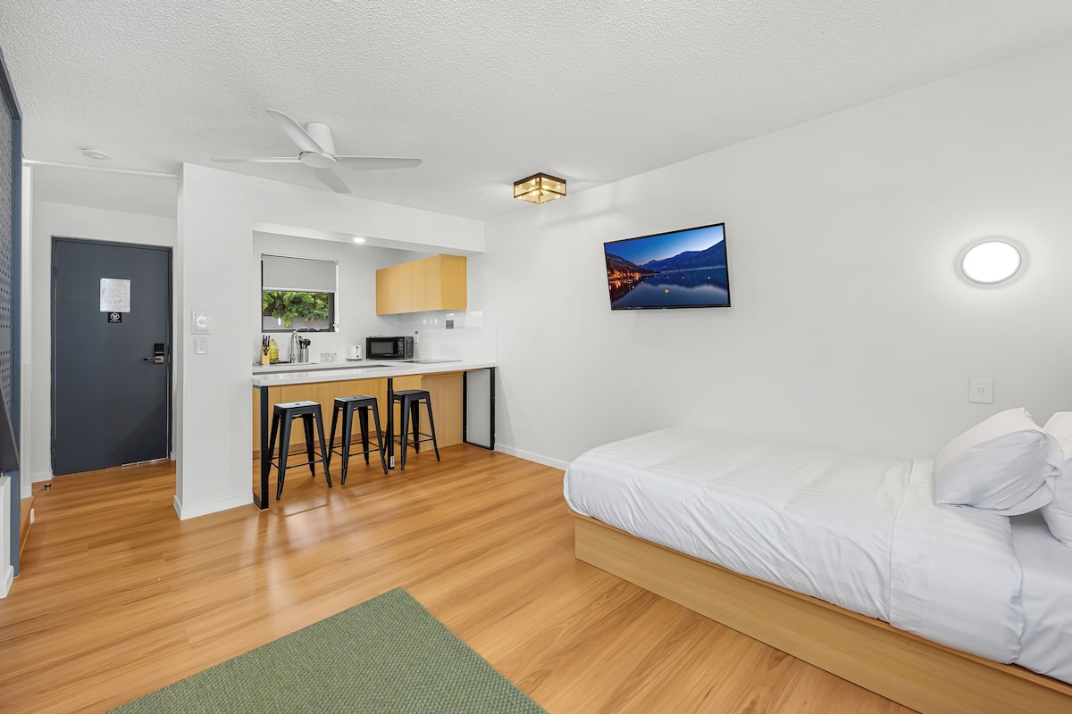 A modern room with a bed, a desk with a computer, and a small kitchen area.