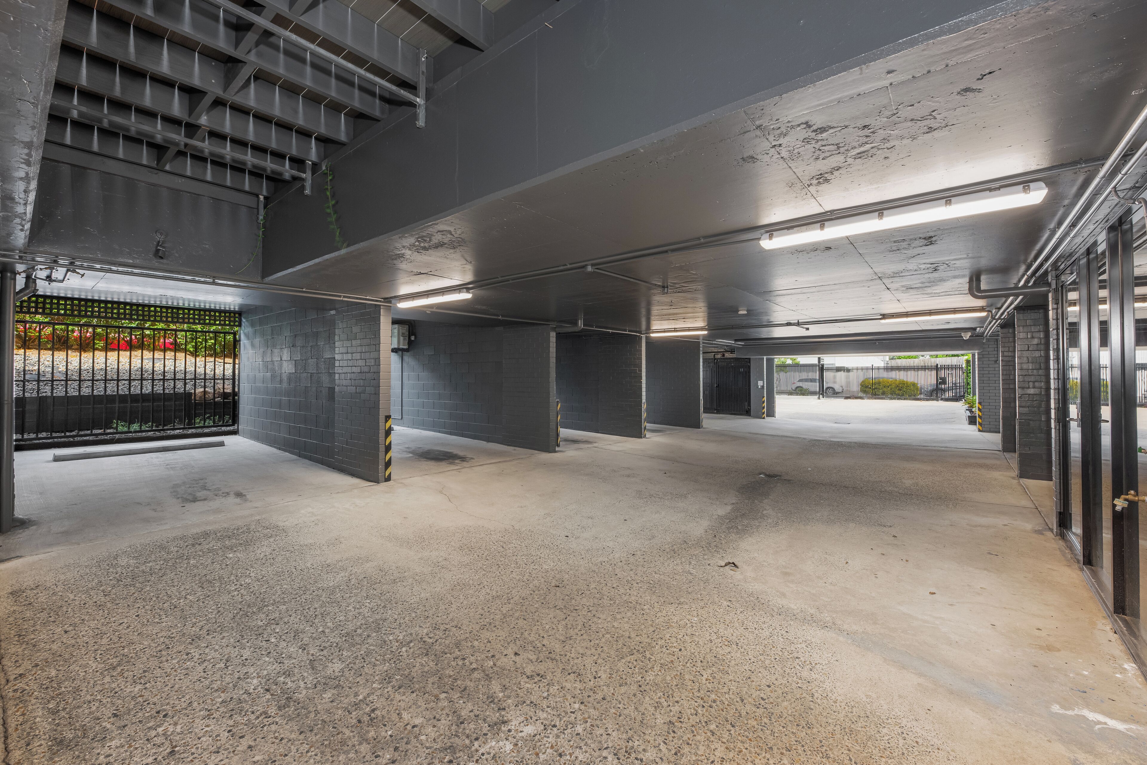 Een parkeergarage binnenshuis met betonnen vloeren en wanden, metalen hekwerken en tl-verlichting.