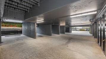 Un parking intérieur avec des planchers et des murs en béton, des garde-corps en métal et un éclairage fluorescent au plafond.