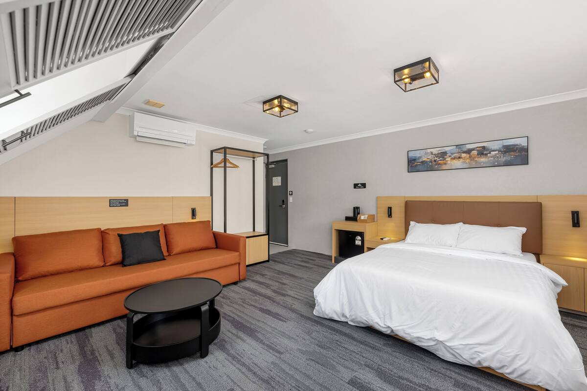 A hotel room with a bed, a sofa, a small table, and a painting on the wall.