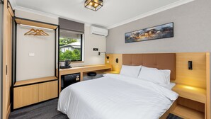 A modern hotel room with a large bed, a desk with a computer, a small kitchenette, and a window with a view of greenery. - Spring Hill Inn (Spring Hill)