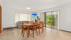 A dining area with a wooden table and chairs, a bench, and a TV on the wall. - Forster holiday home, linen included-WiFi- pets welcome-cafes,beach, golf, fish  (Forster)